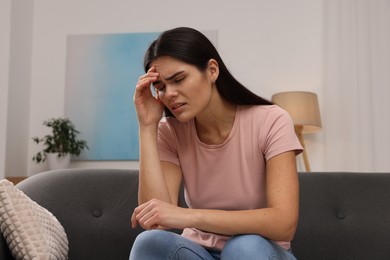 Sad woman suffering from headache on sofa indoors