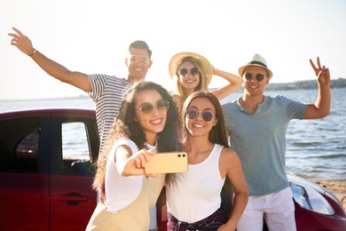 Photo of Happy friends taking selfie near car on beach. Summer trip