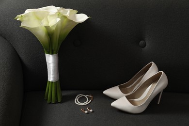Photo of Beautiful calla lily flowers tied with ribbon, shoes and jewelry on sofa