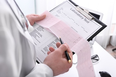 Doctor examining cardiogram in medical clinic, closeup