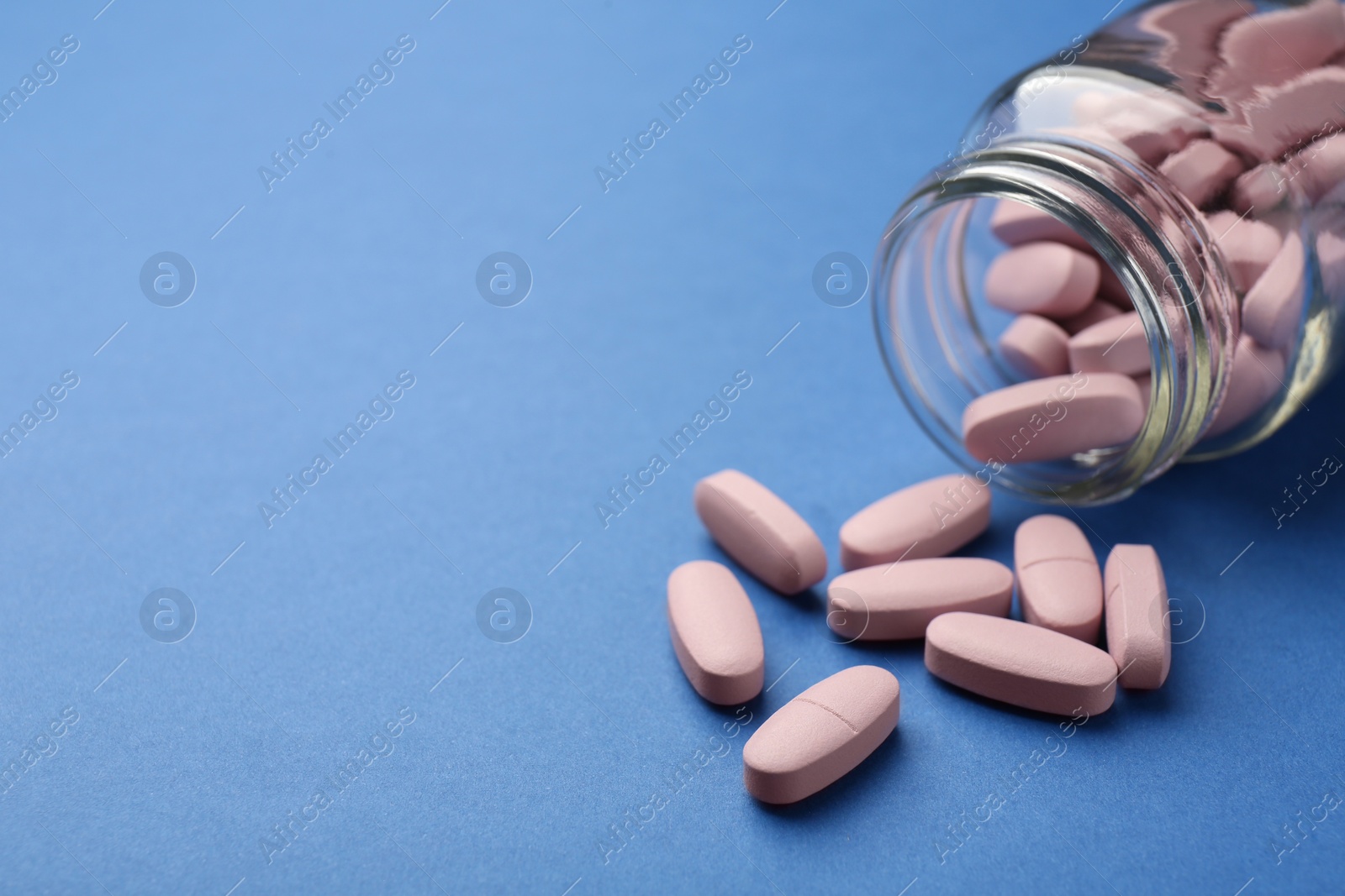 Photo of Bottle of pink vitamin capsules on blue background, closeup. Space for text