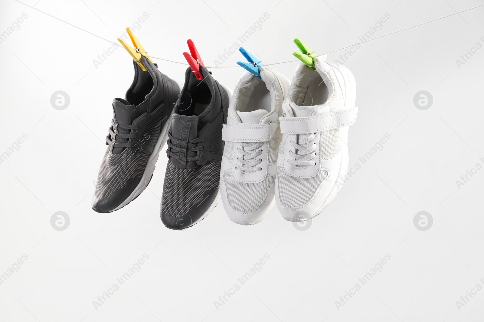 Photo of Different stylish sneakers drying on washing line against light grey background