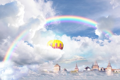 Image of Fantasy world. Beautiful rainbow and hot air balloon in sky with fluffy clouds over enchanted castle