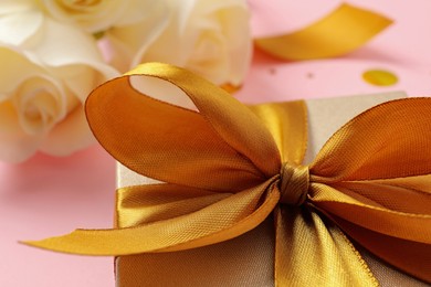 Photo of Beautiful golden gift box with bow on pink background, closeup