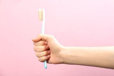 Woman holding toothbrush with natural bristles on pink background, closeup