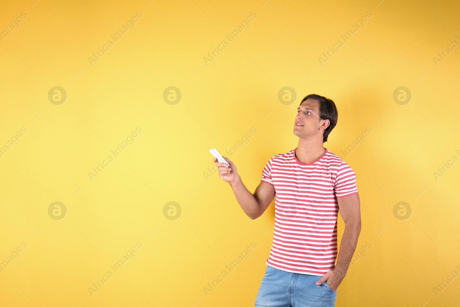 Photo of Young man with air conditioner remote on color background, copy space text