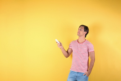 Young man with air conditioner remote on color background, copy space text