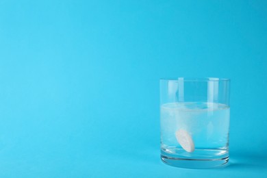 Photo of Glass of water with effervescent tablet on light blue background, space for text