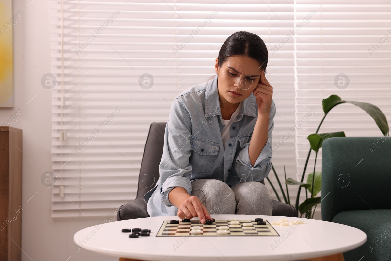 Photo of Thoughtful woman playing checkers in armchair at home