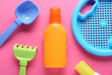 Photo of Bottle of suntan cream and children's beach toys on pink background, flat lay