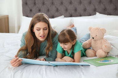 Photo of Young woman and her daughter reading book in bedroom. Helping to learn
