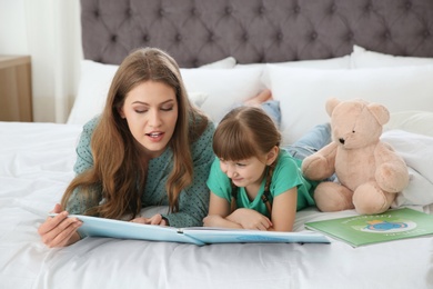 Young woman and her daughter reading book in bedroom. Helping to learn