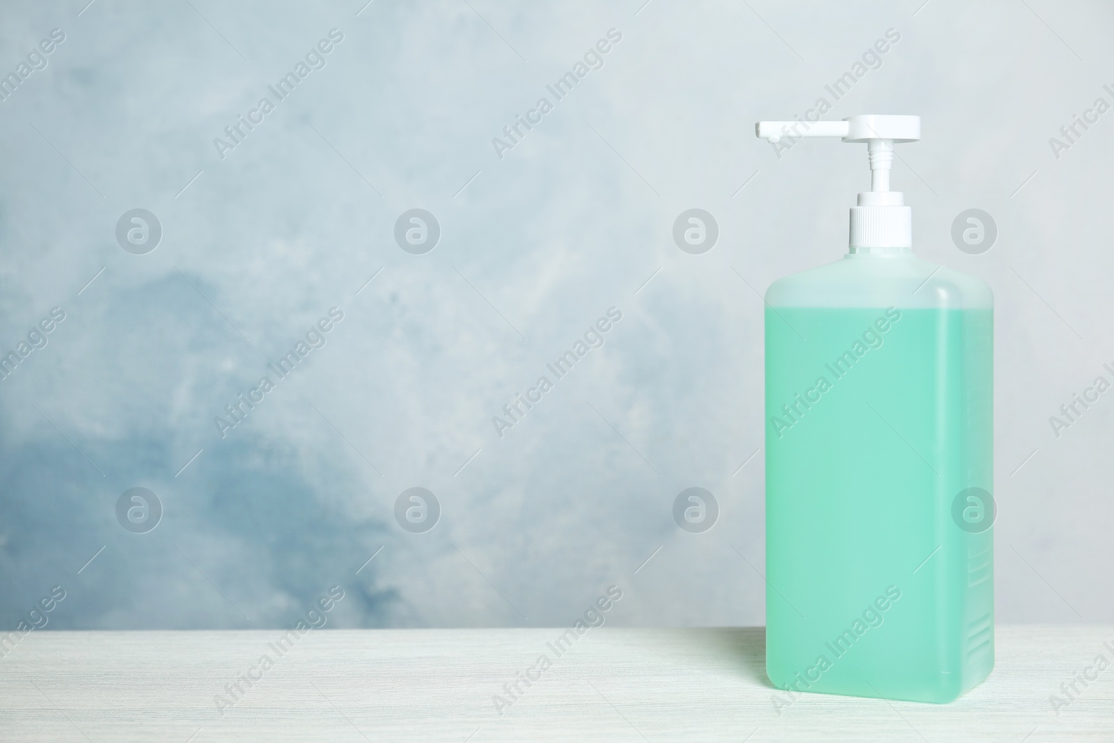 Photo of Dispenser bottle with green antiseptic gel on table against light background. Space for text