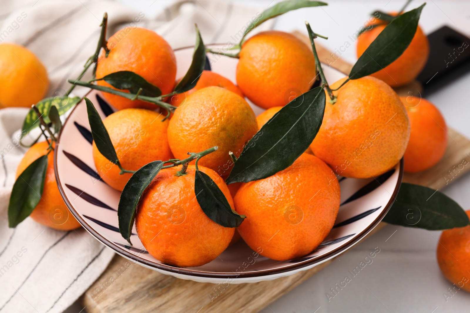 Photo of Fresh ripe tangerines with green leaves in bowl on white table, closeup