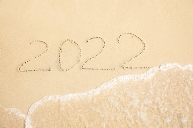 Photo of Sandy beach with written 2022 washed by sea. Happy New Year, above view