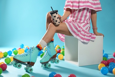 Photo of Young woman with retro roller skates and cup of drink on color background, closeup. Space for text