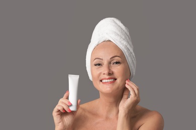 Portrait of beautiful mature woman with perfect skin holding tube of cream on grey background