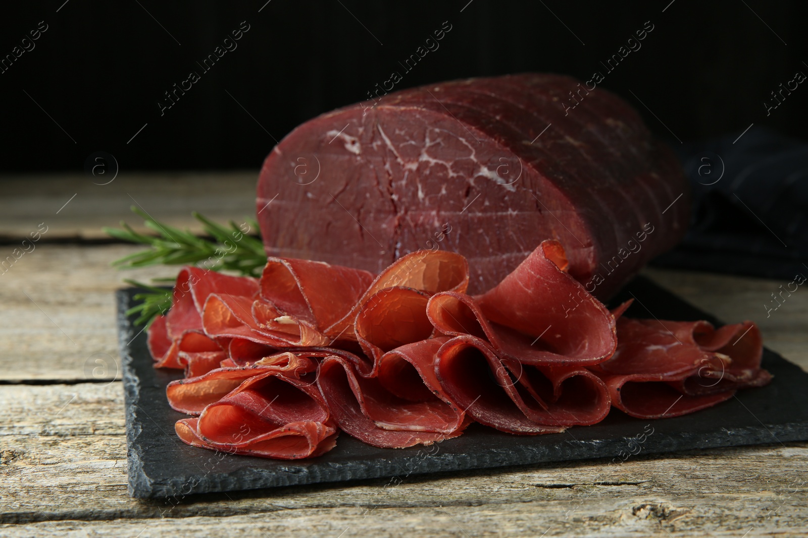 Photo of Tasty bresaola and rosemary on wooden table, closeup