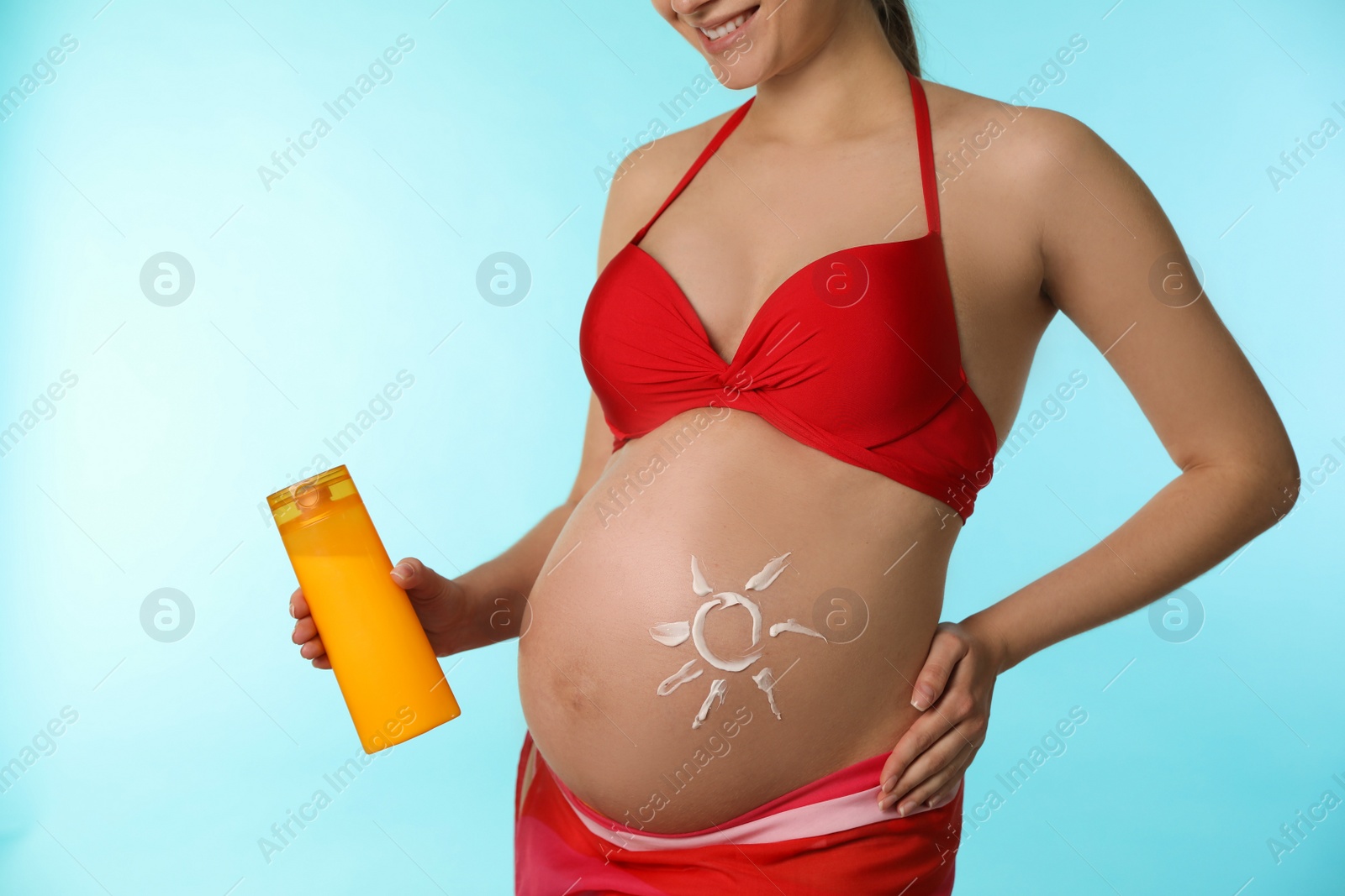 Photo of Young pregnant woman with sun protection cream on light blue background, closeup