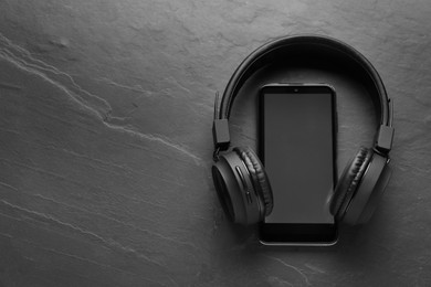 Smartphone with blank screen and headphones on grey textured background, top view with space for text. Sound equipment