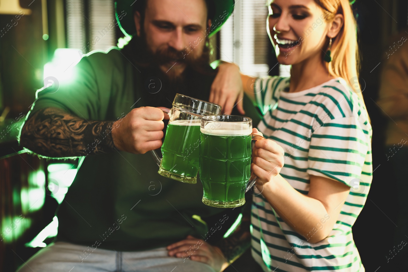 Photo of Young woman and man toasting with green beer in pub, focus on glasses. St. Patrick's Day celebration