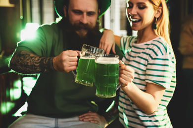 Photo of Young woman and man toasting with green beer in pub, focus on glasses. St. Patrick's Day celebration