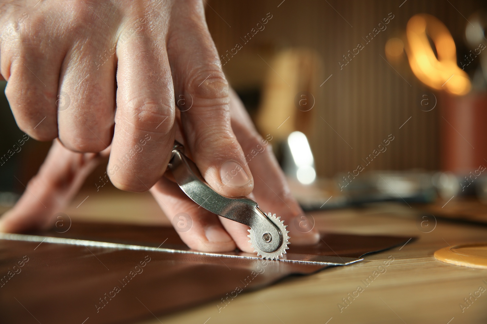 Photo of Man marking leather with roller in workshop, closeup