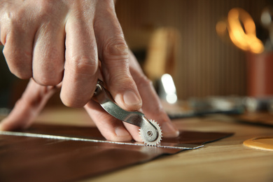 Photo of Man marking leather with roller in workshop, closeup