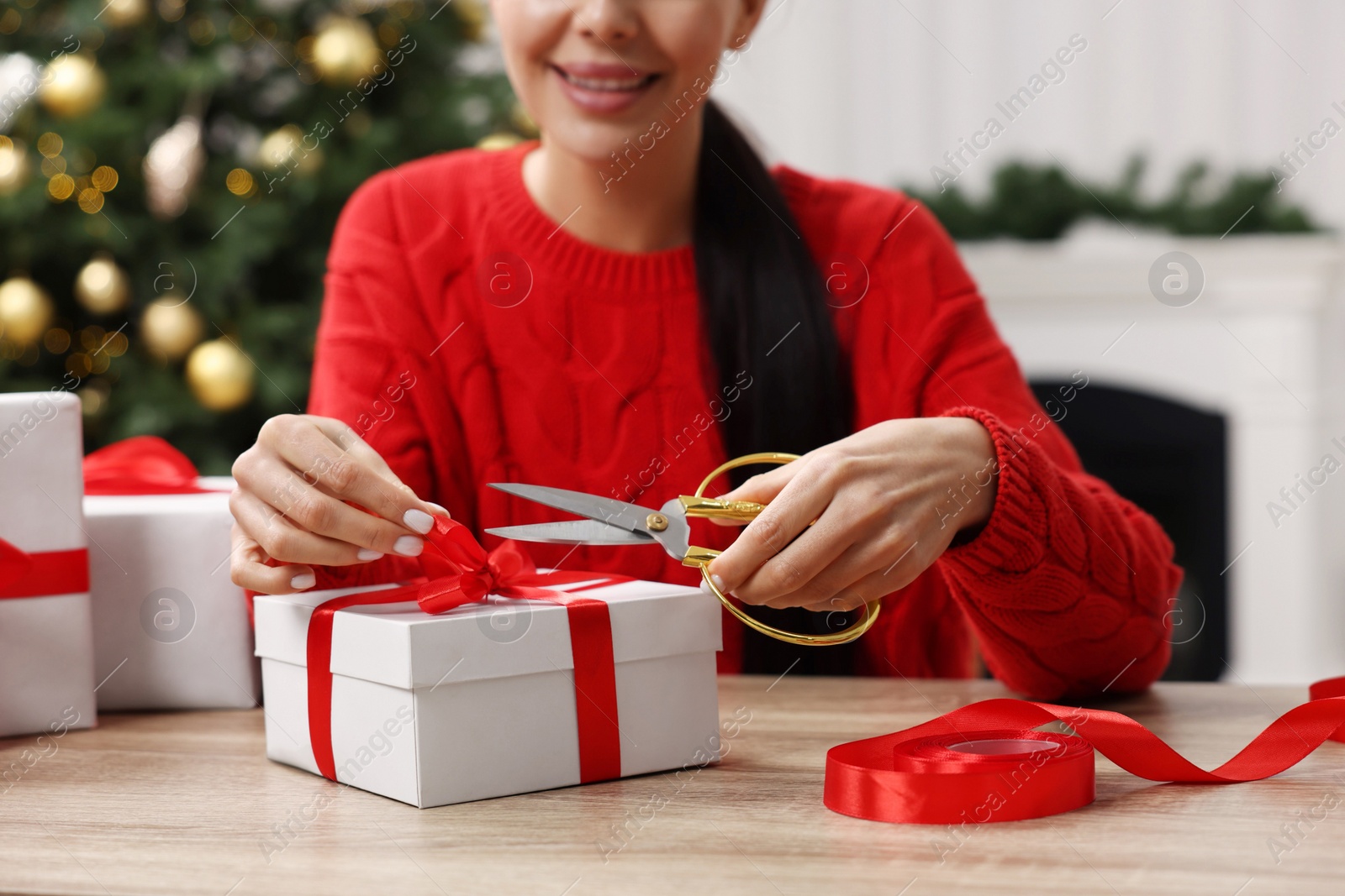 Photo of Woman decorating Christmas gift box at wooden table in room, closeup