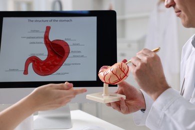 Gastroenterologist with human stomach model consulting patient at table in clinic, closeup
