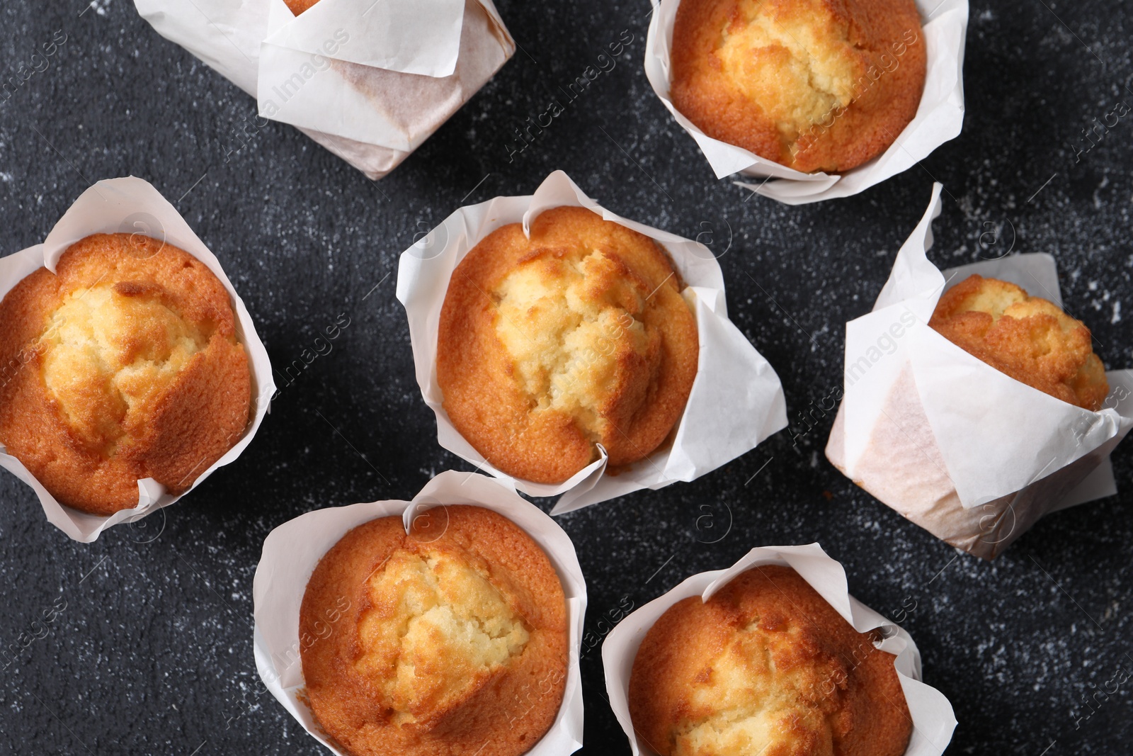 Photo of Delicious sweet muffins on black textured table, flat lay