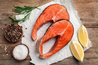 Fresh salmon steaks with spices, lemon and rosemary on wooden table, flat lay