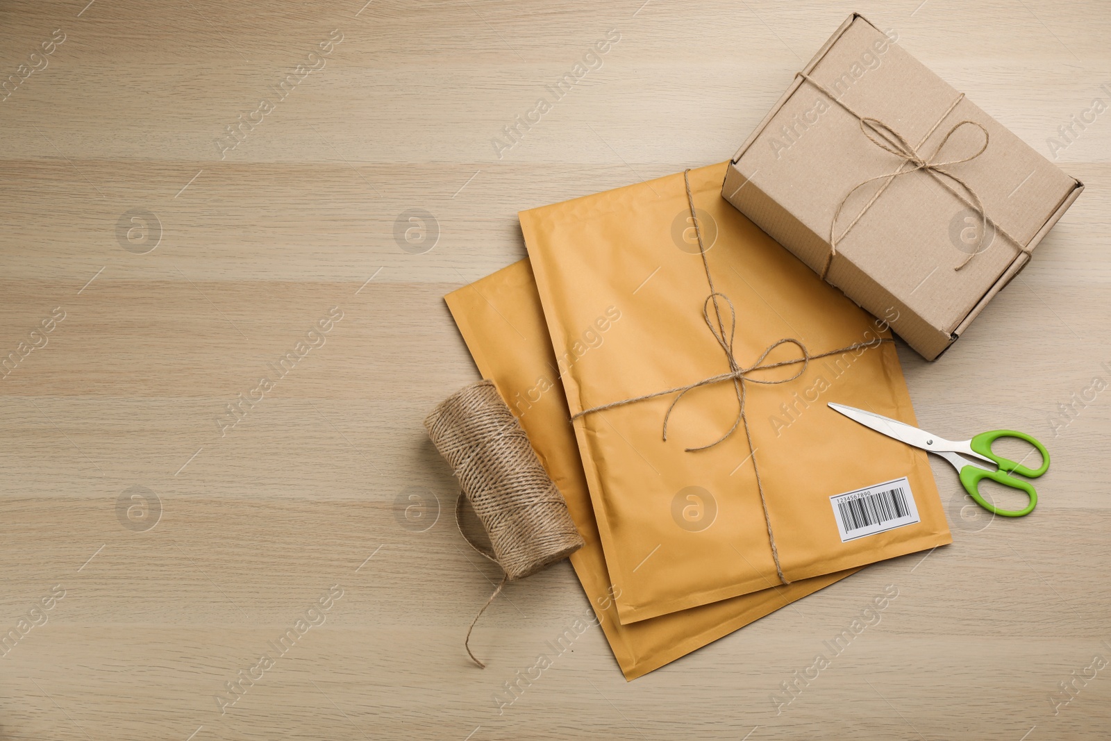 Photo of Padded envelopes, box, rope and scissors on wooden background, flat lay. Space for text