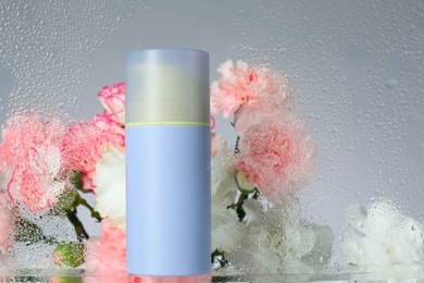 Bottle with moisturizing cream and beautiful flowers on light background, view through wet glass