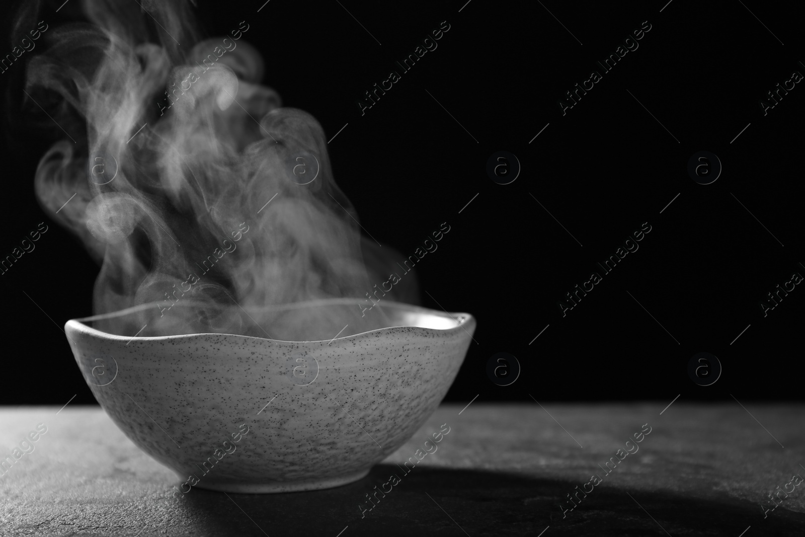 Photo of Bowl with steam on table against black background. Space for text
