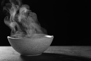 Bowl with steam on table against black background. Space for text