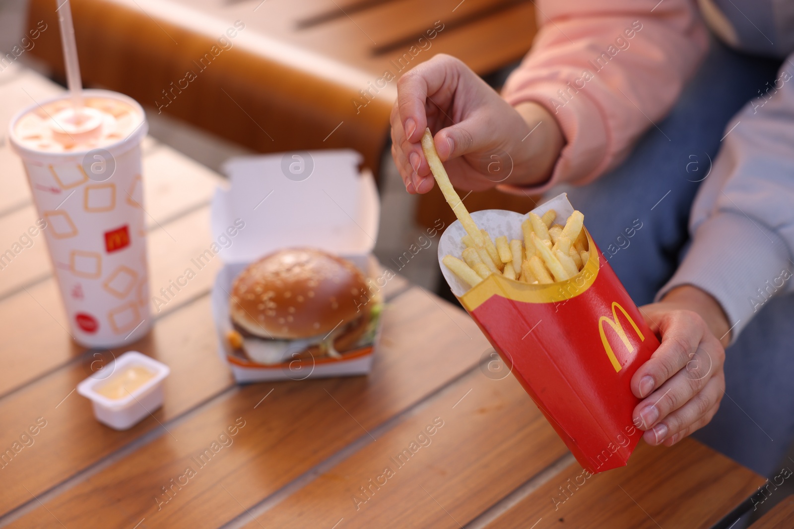 Photo of Lviv, Ukraine - September 26, 2023: Woman eating McDonald's menu at wooden table outdoors, closeup