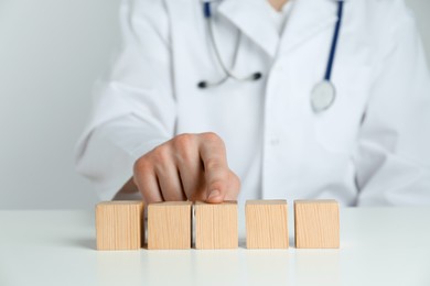 Photo of Doctor arranging blank wooden cubes on white table against light background, closeup. Space for text