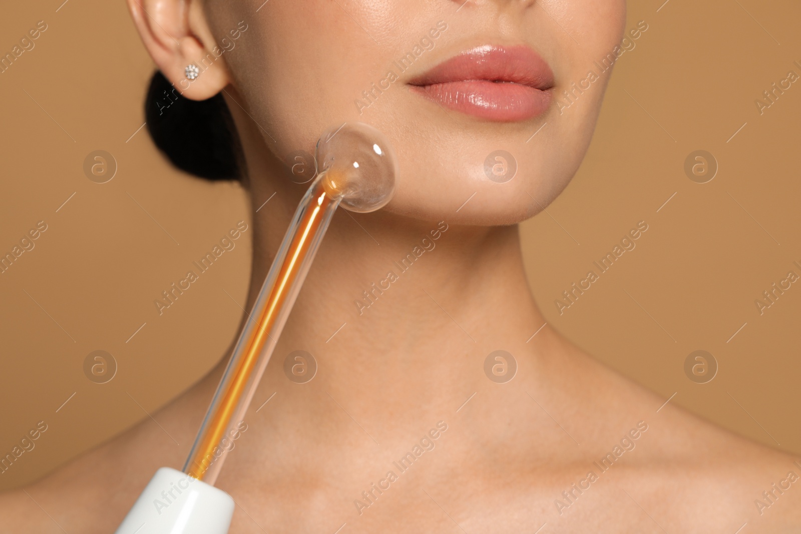 Photo of Woman using high frequency darsonval device on beige background, closeup