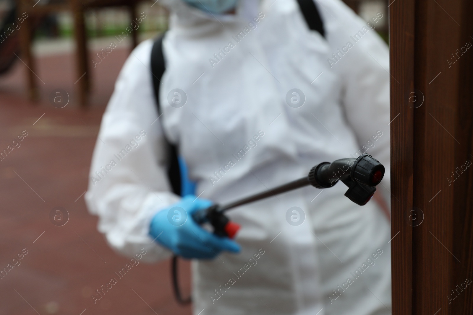 Photo of Woman wearing chemical protective suit at playground, focus on disinfectant sprayer. Preventive measure during coronavirus pandemic