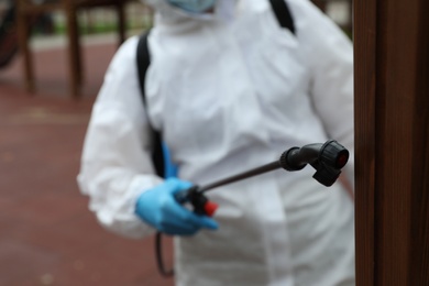 Woman wearing chemical protective suit at playground, focus on disinfectant sprayer. Preventive measure during coronavirus pandemic