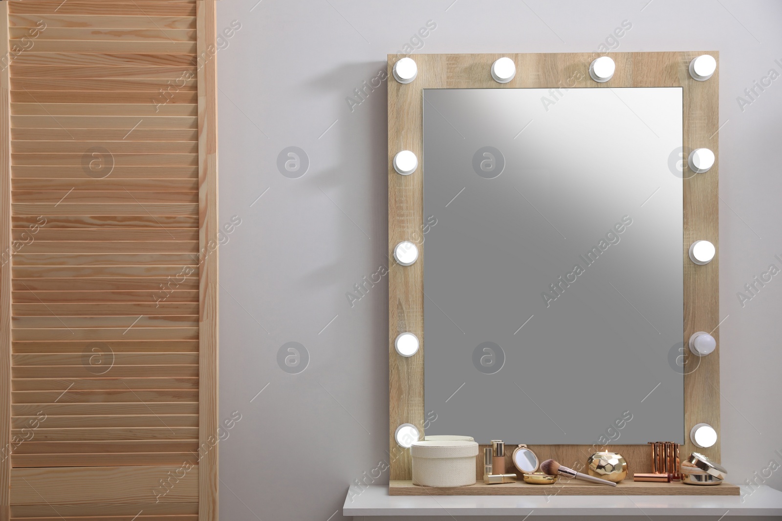 Photo of Stylish dressing table with cosmetics, mirror and accessories near white wall