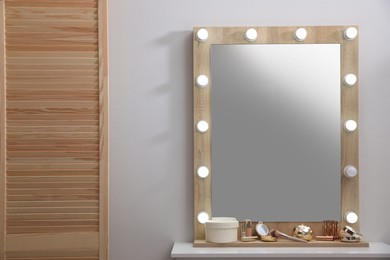 Photo of Stylish dressing table with cosmetics, mirror and accessories near white wall