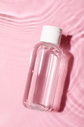 Photo of Wet bottle of micellar water on pink background, top view