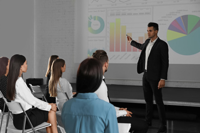 Male business trainer giving lecture in conference room with projection screen