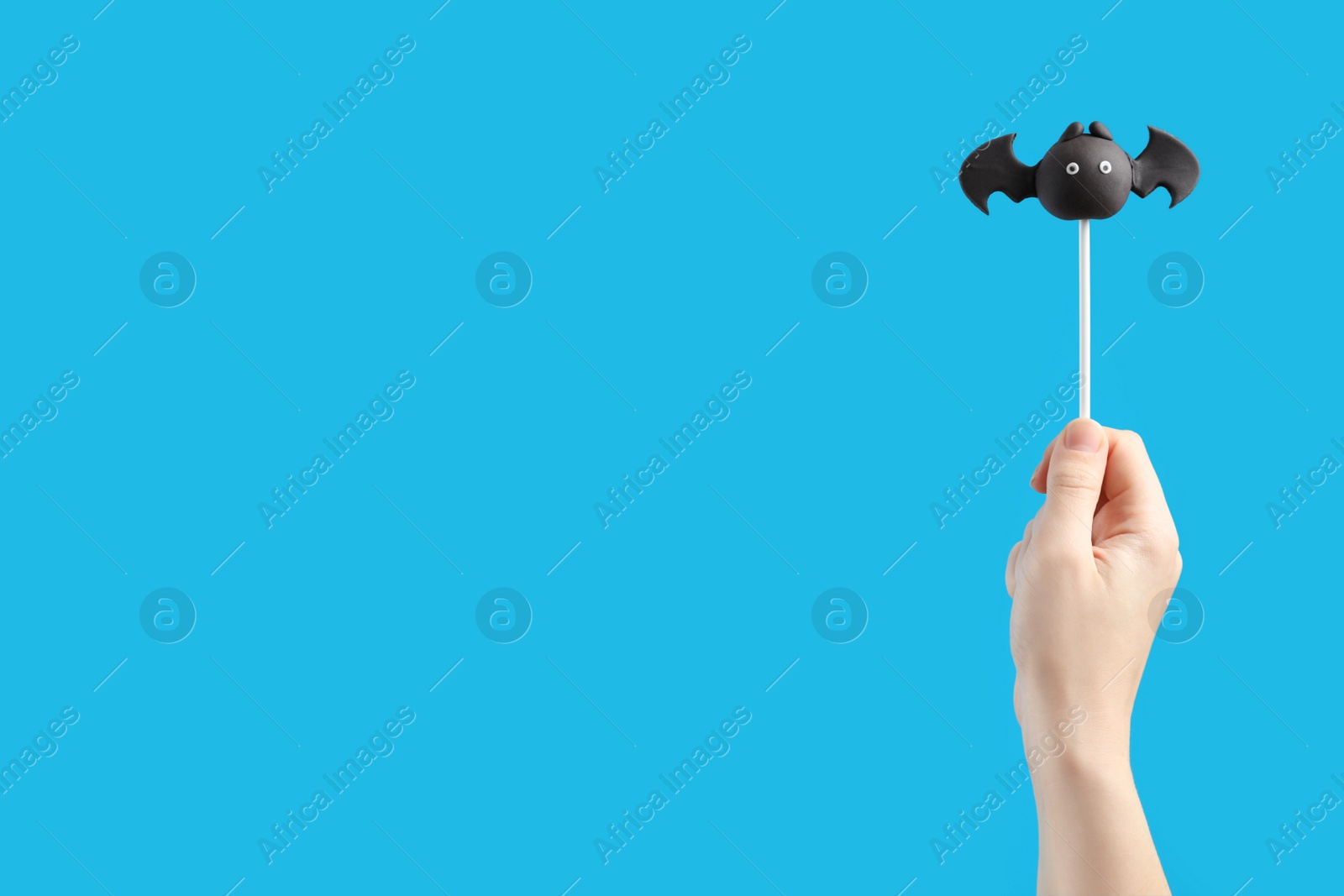 Photo of Woman with delicious bat shaped cake pop and space for text on light blue background, closeup. Halloween celebration