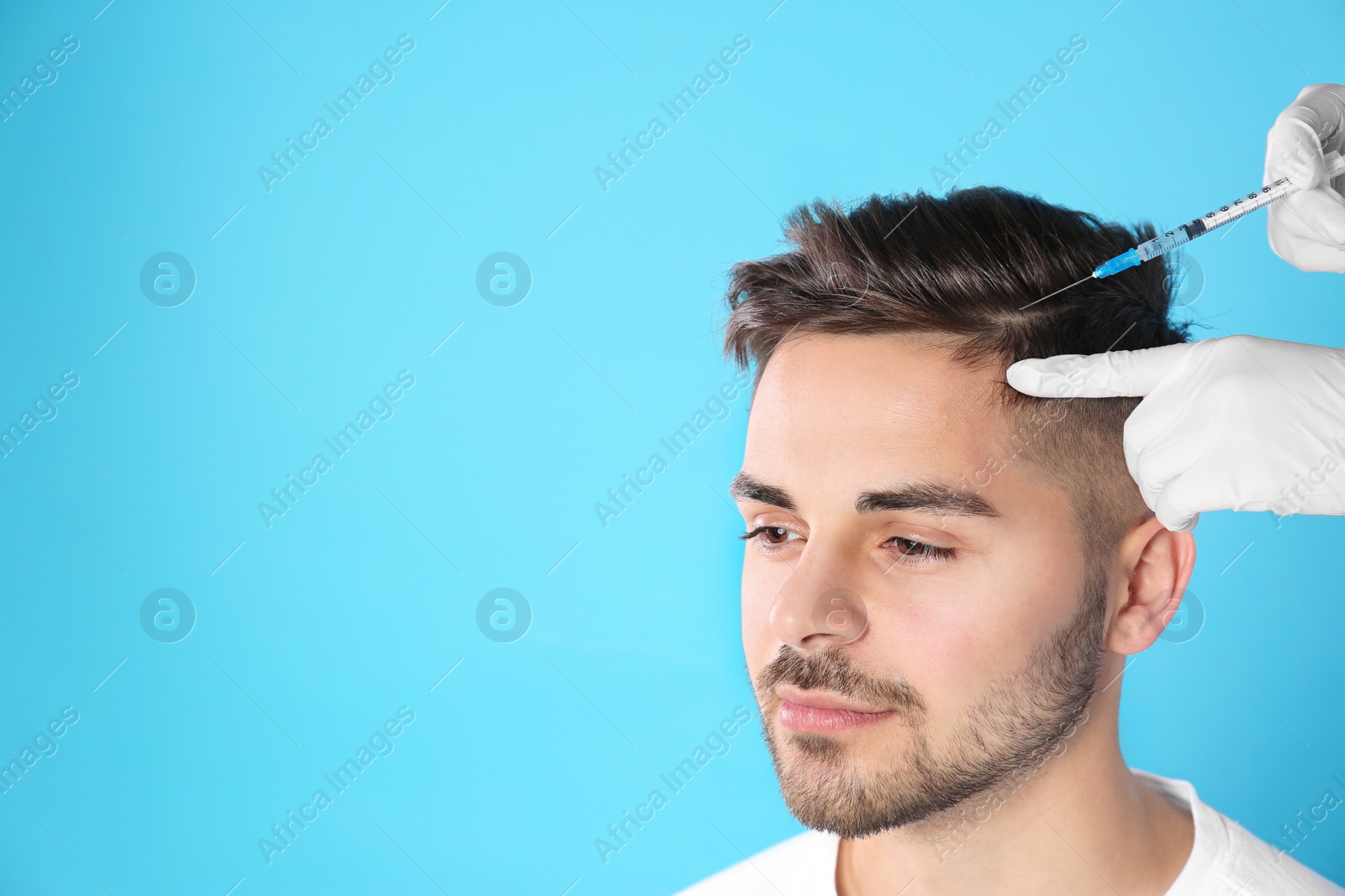 Photo of Young man with hair loss problem receiving injection on color background. Space for text