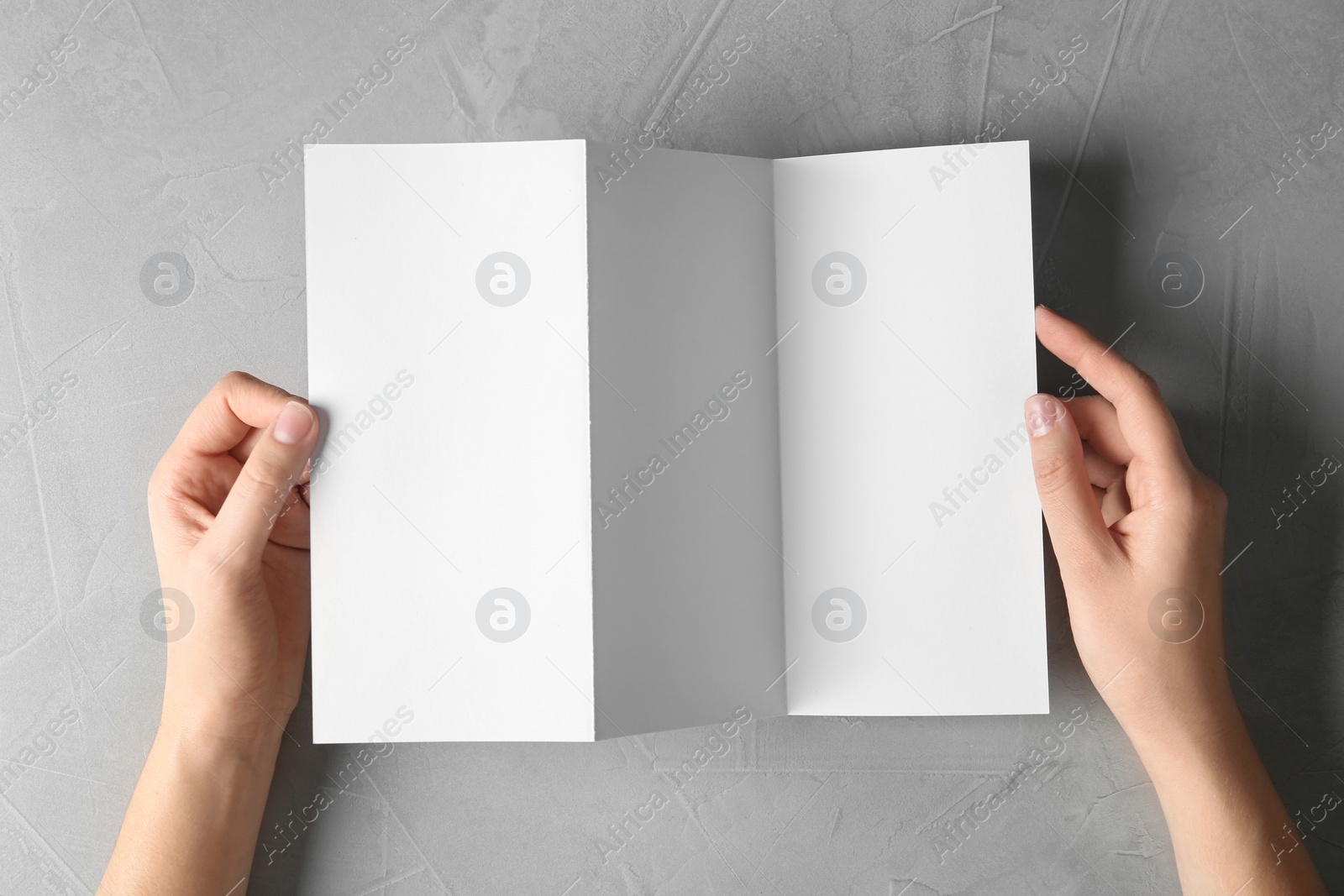 Photo of Woman holding blank brochure mock up on light background, top view