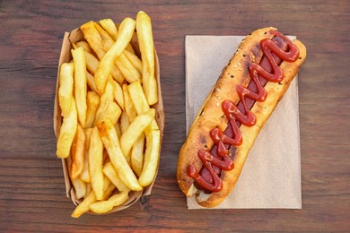 Photo of Fresh tasty hot dog and french fries on wooden table, flat lay