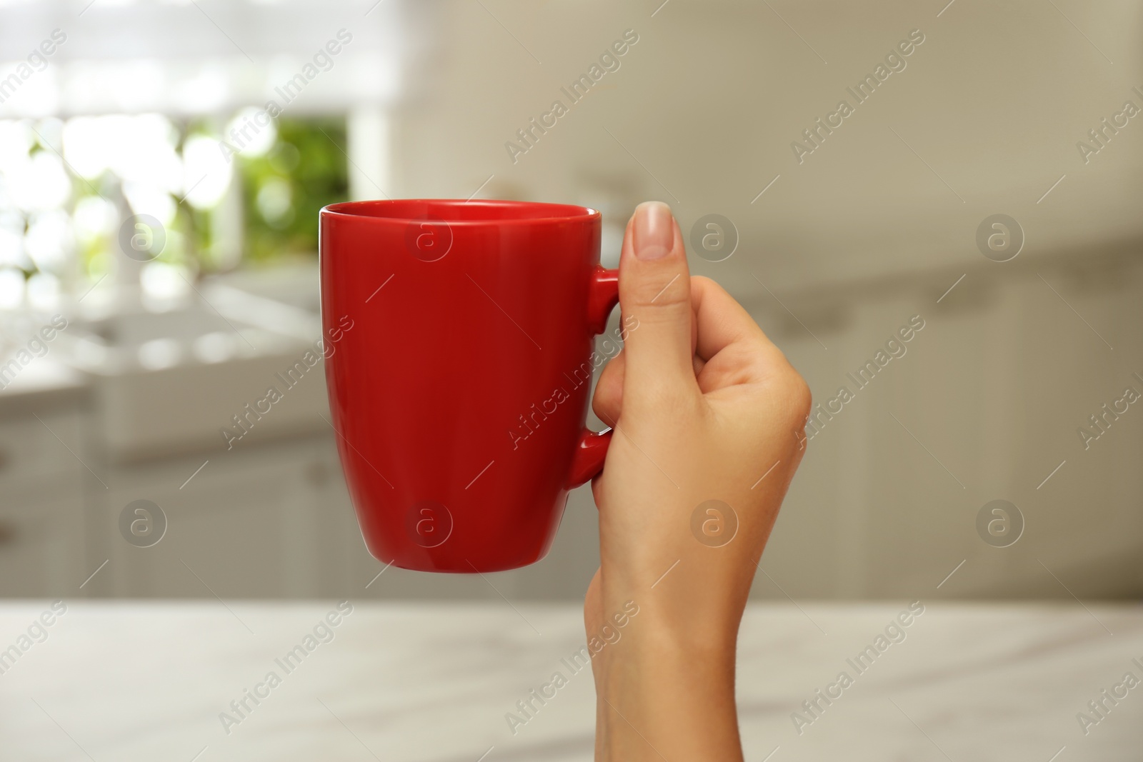 Photo of Woman holding elegant red cup in kitchen, closeup